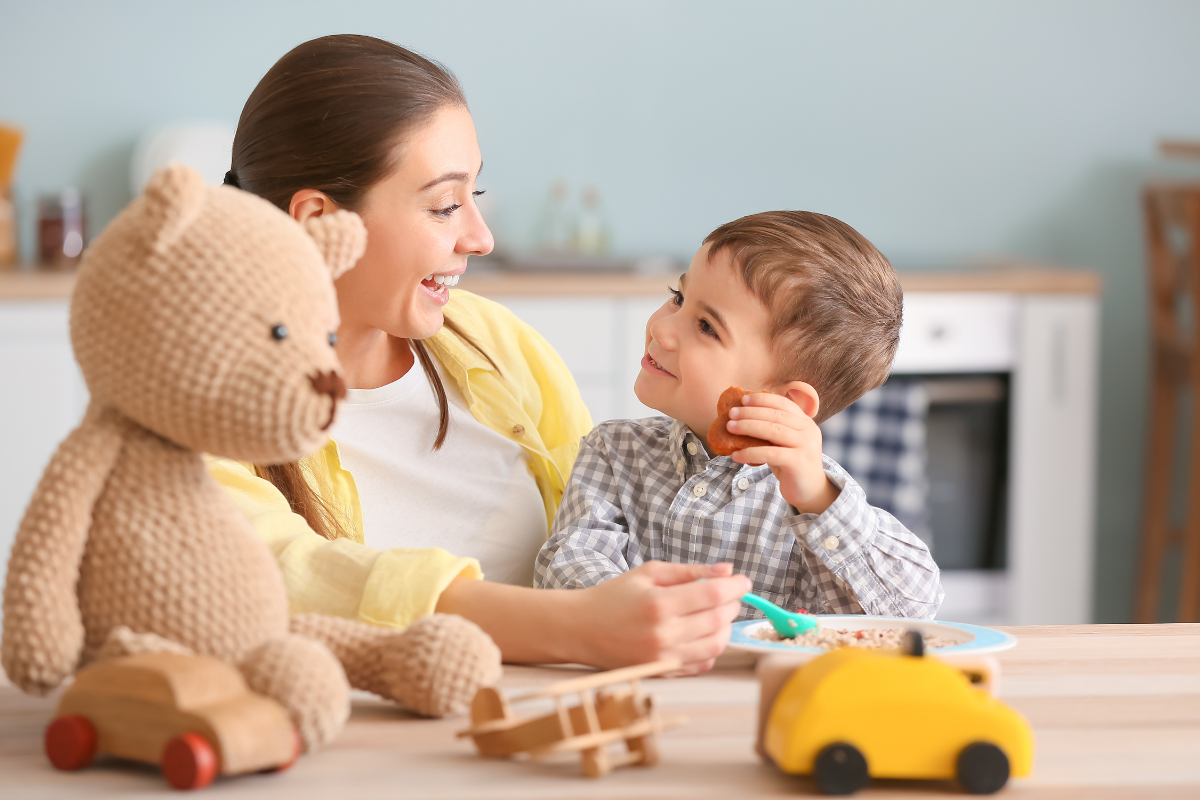 Nanny with child feeding him oatmeal with toys on the table