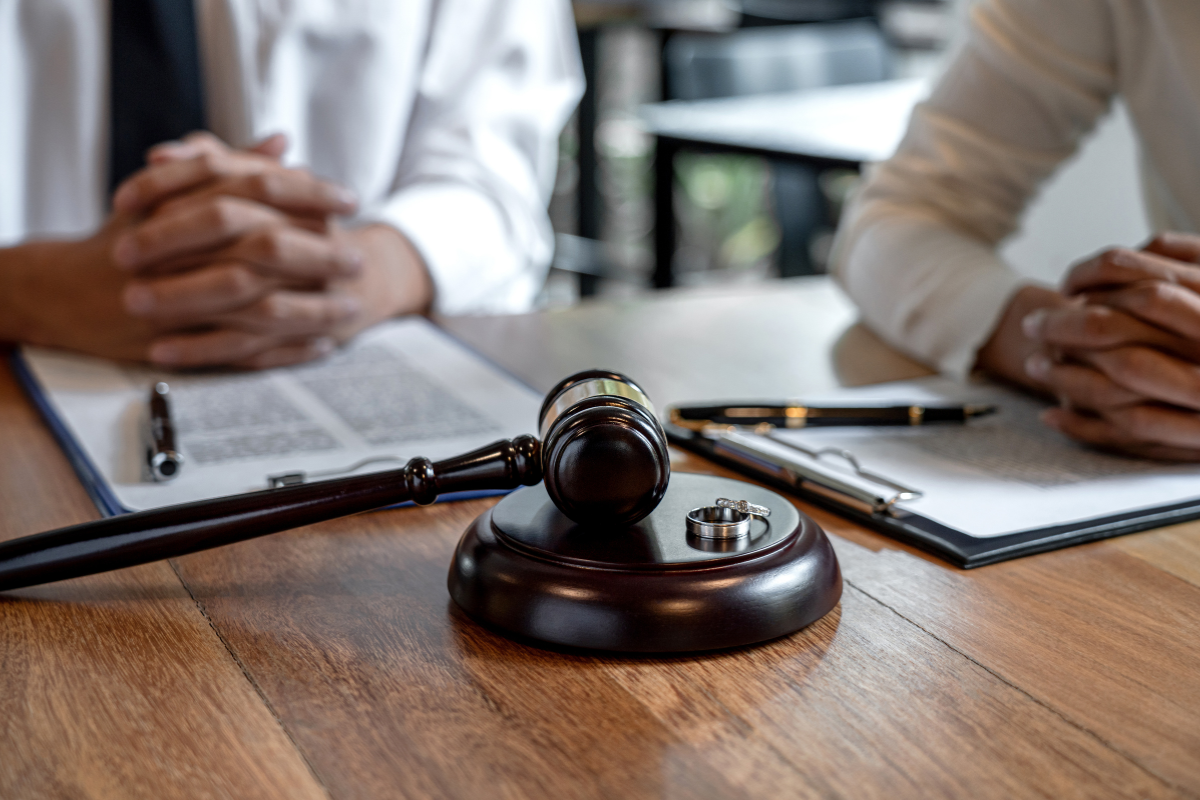 Can I Buy Out Alimony Payments in Maryland or D.C. man and woman sitting at a table with arms crossed. they have papers in front of them, a gavel, and their wedding rings on the table.
